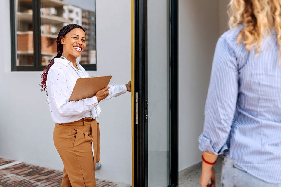 A professional woman holding a door open for a client.