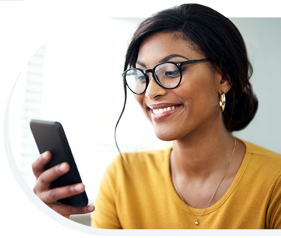 A smiling woman wearing a yellow shirt, glasses, and looking at her phone.