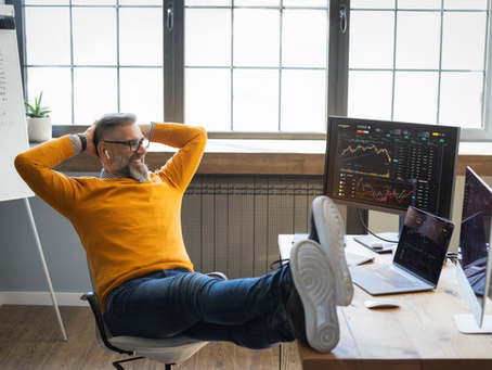A man reclined in an office chair, looking at his desk's computer screens.